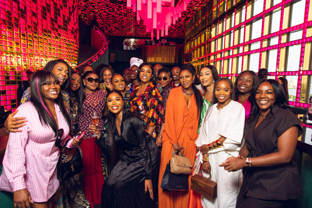 A joyful gathering of diverse women posing together in a vibrant venue adorned with colorful lights.