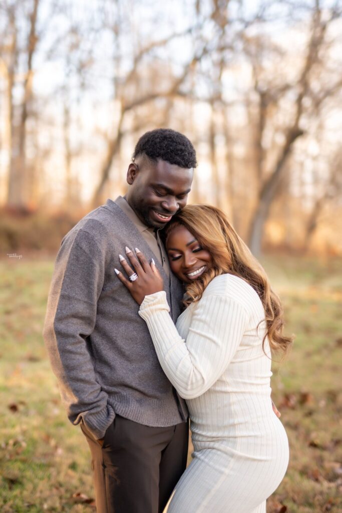 A couple sharing a joyful moment outdoors, smiling while standing close together, surrounded by soft, blurred natural scenery.