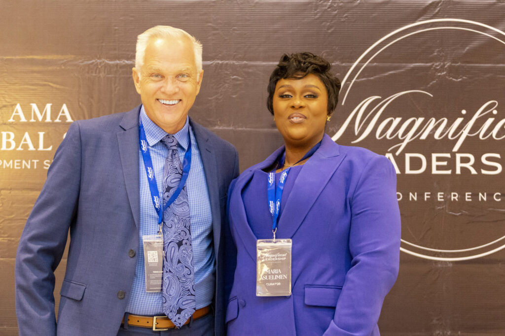 Two smiling attendees posing together at a conference, with a backdrop featuring the event's branding.